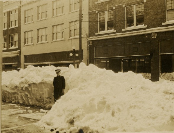 A 14-year-old young man stands in front of a wall of plowed snow that reaches his height.