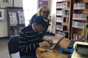 Librarian assists library patron with the use of laptop.