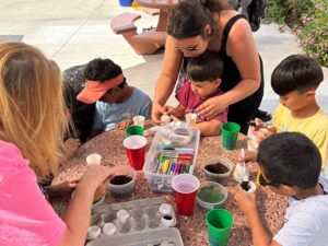 Children with the help of parents are planting grass seeds in eggshells, soil, and water