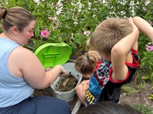 The librarian is showing two children the worms and soil in a bucket.